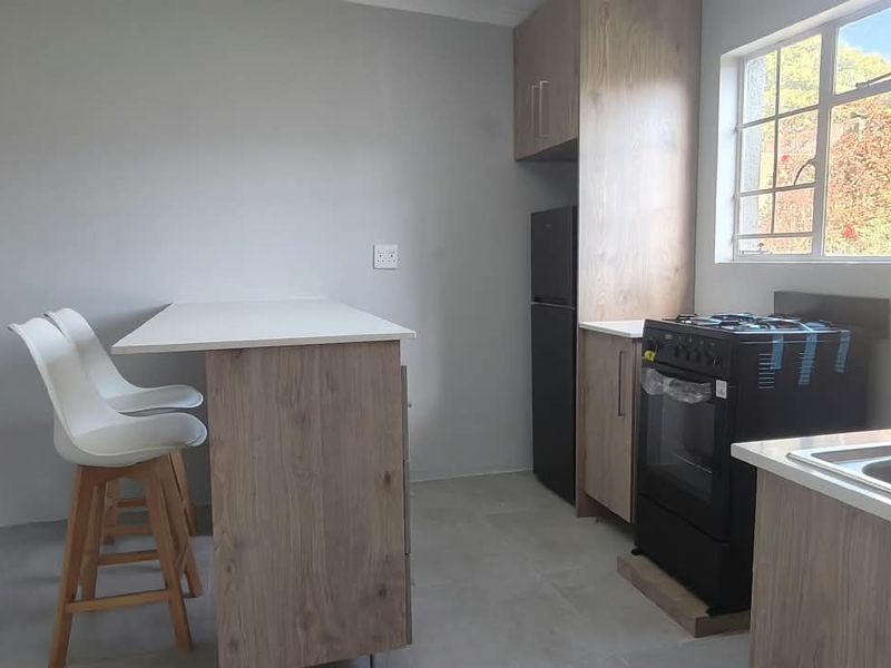 A modern, compact kitchen featuring wood-finish cabinetry, a gas stove with oven, stainless steel sink, and a breakfast bar area with tiled flooring.