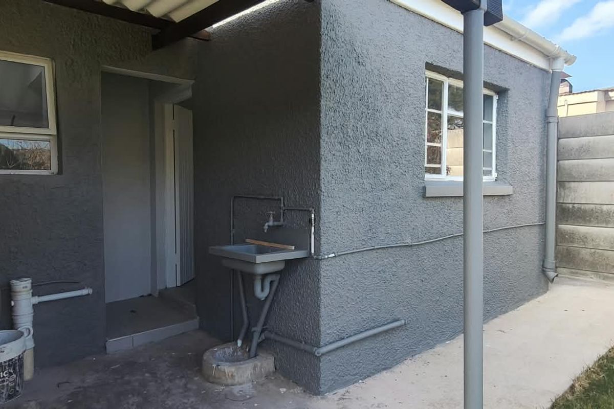 Rear exterior view of the cottage featuring a utility sink, concrete pathway, and precast boundary walling.