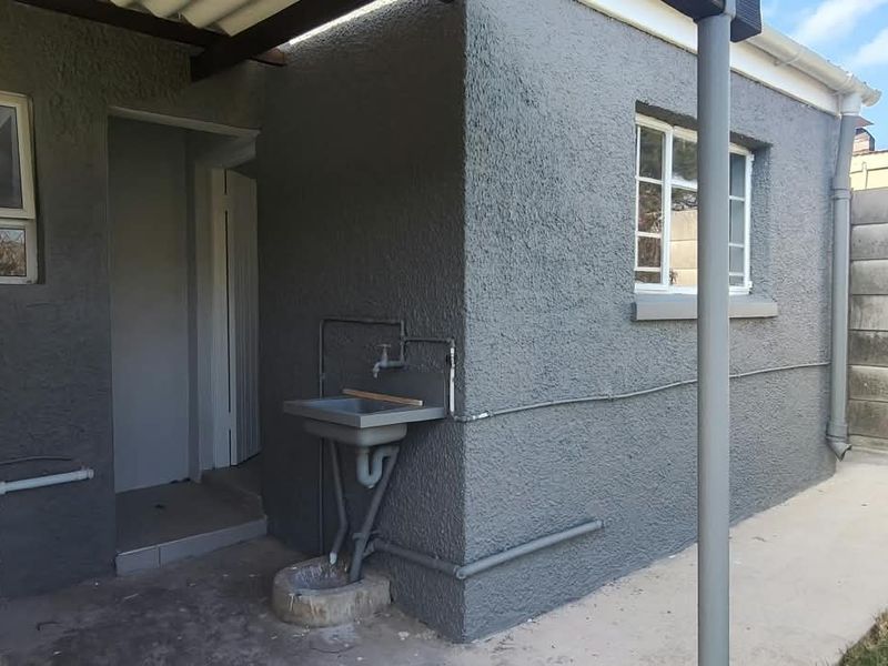 Rear exterior view of the cottage featuring a utility sink, concrete pathway, and precast boundary walling.