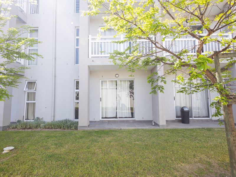Rear view of the apartment building featuring ground floor patios with sliding glass doors and upper level balconies with white railings.