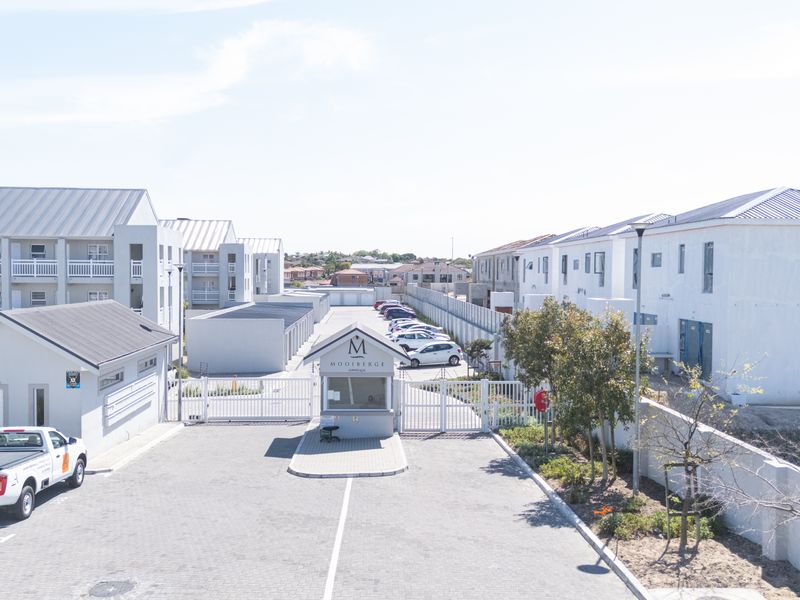 Aerial view of the apartment complex entrance featuring a secure gated access point, guard house, and paved driveway with surrounding perimeter walls.