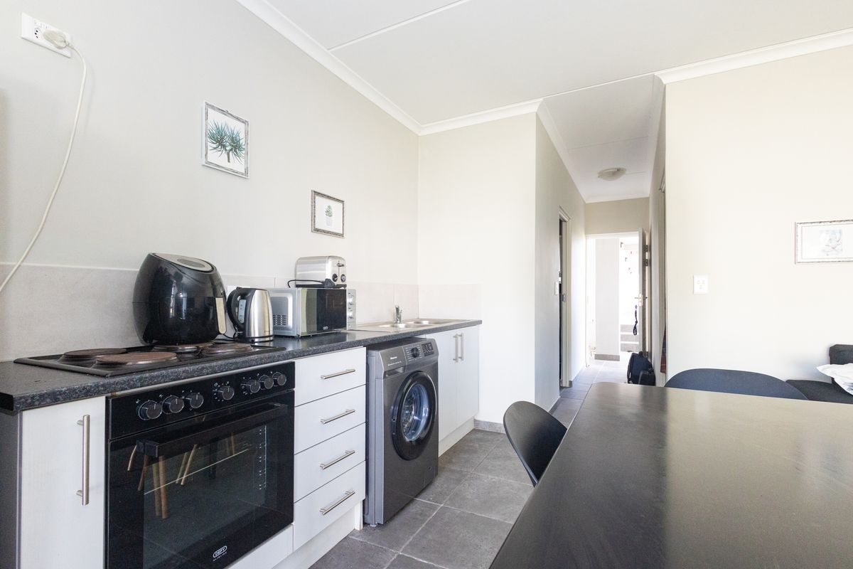 Compact kitchen featuring built-in cabinetry, electric oven and hob, stainless steel sink, and tiled flooring, with direct access to the hallway.