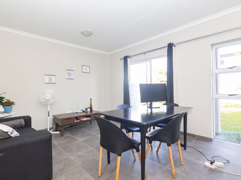 A functional living area featuring tiled flooring, neutral walls, and direct access to the garden through a sliding glass door.