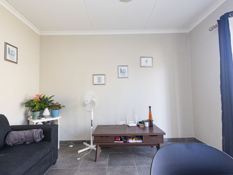 A living room area featuring neutral wall tones, tiled flooring, and coved ceiling details, providing a functional and well-lit space.