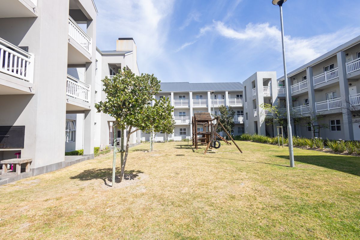 A view of the apartment complex's communal garden area, featuring landscaped lawns, balconies, and outdoor braai facilities for residents.