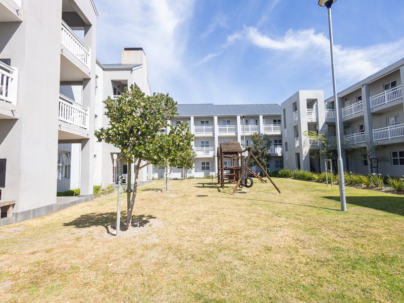 A view of the apartment complex's communal garden area, featuring landscaped lawns, balconies, and outdoor braai facilities for residents.