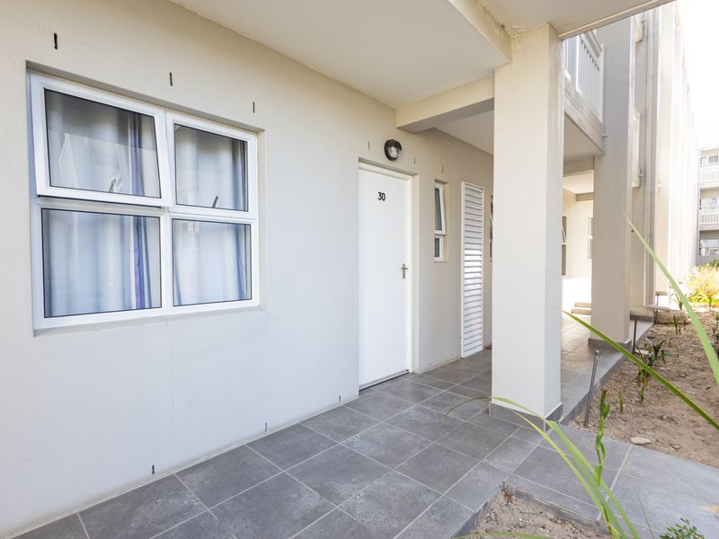 Exterior view of an apartment entrance featuring a tiled walkway, aluminium window frames, and a secure front door.
