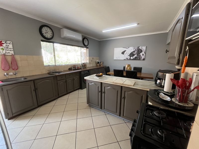Open-plan kitchen and dining area featuring dark cabinetry, a central island, tiled flooring, and a wall-mounted air conditioning unit.