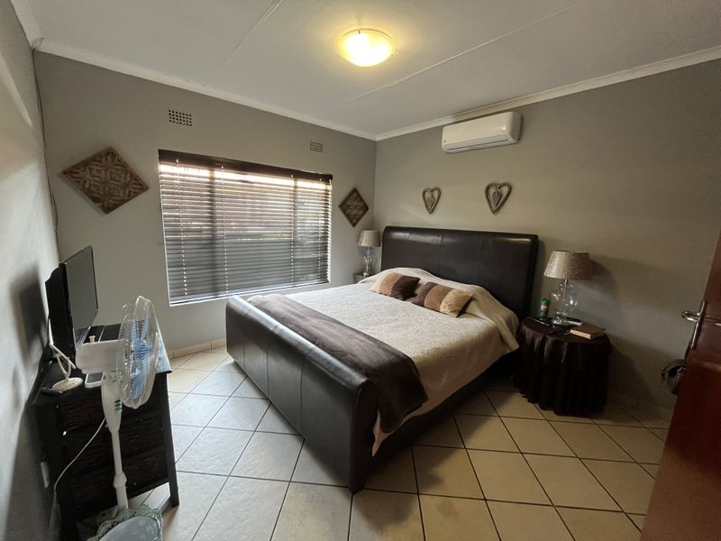 A functional bedroom featuring tiled flooring, an integrated air conditioning unit, and venetian blinds for privacy.