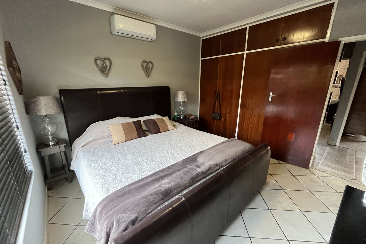 A bedroom featuring built-in wooden cupboards, tiled flooring, and a wall-mounted air conditioning unit.