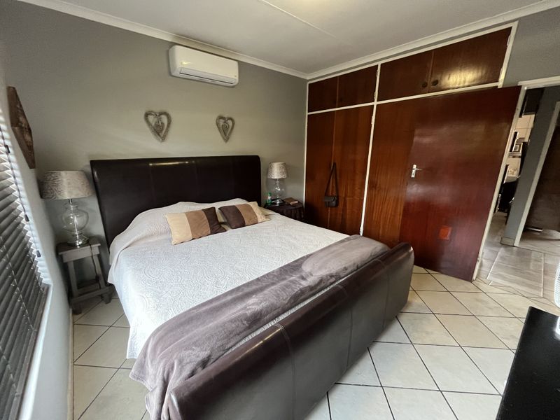 A bedroom featuring built-in wooden cupboards, tiled flooring, and a wall-mounted air conditioning unit.