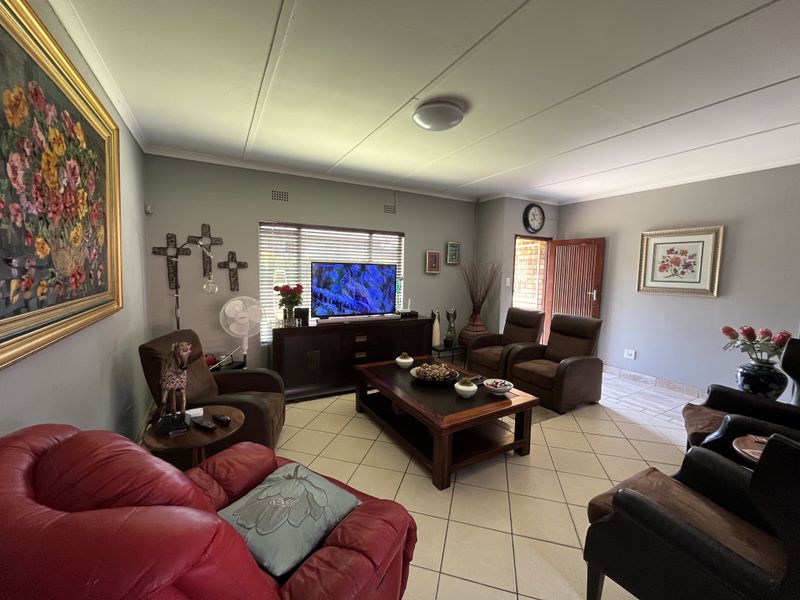 A spacious living room featuring neutral wall tones, tiled flooring, and natural light through venetian blinds, providing a comfortable and functional family area.