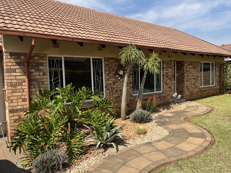 A well-maintained single-story home featuring a face brick facade, tiled roof, and a curved paved walkway leading to the entrance.