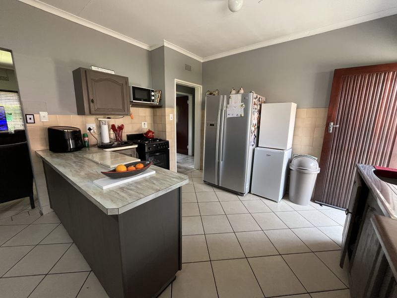 A functional kitchen featuring tiled flooring, a tiled backsplash, built-in cabinetry, and a central island with a laminate countertop.