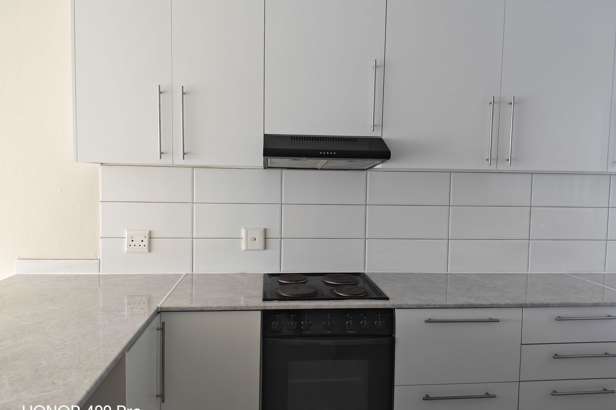 A clean, modern kitchen featuring white cabinetry, stone-look countertops, a subway tile backsplash, and integrated electric cooking appliances.