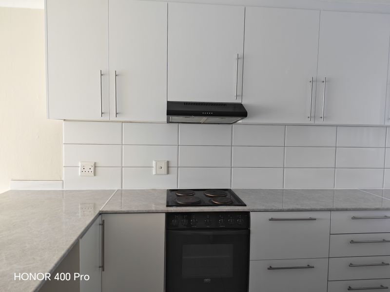 A clean, modern kitchen featuring white cabinetry, stone-look countertops, a subway tile backsplash, and integrated electric cooking appliances.