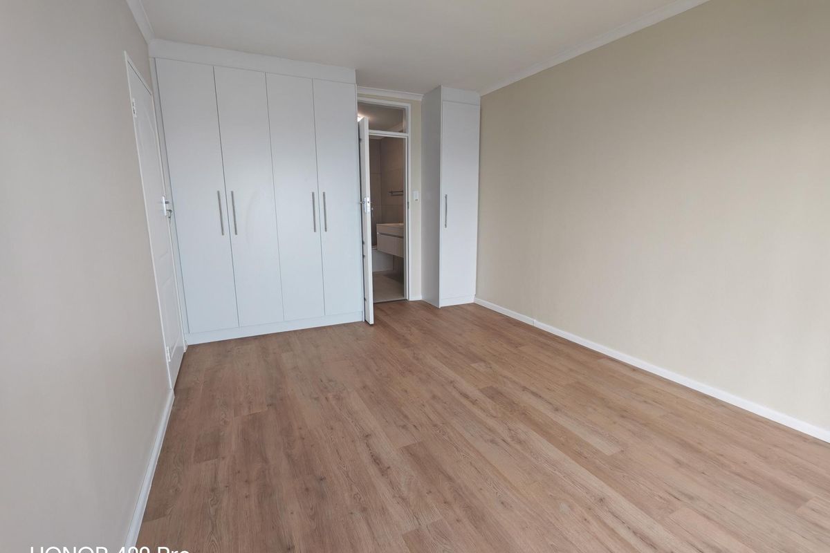 A bright, empty bedroom featuring modern laminate flooring and extensive built-in cupboard storage, with direct access to an en-suite bathroom.