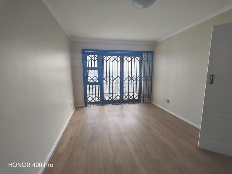 A bright, empty living room featuring modern laminate flooring and a secure sliding door with a fitted security gate.