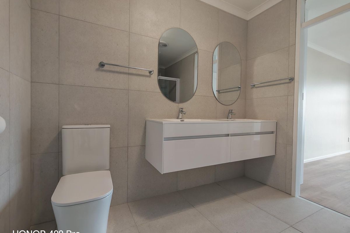 Modern bathroom featuring a double vanity with wall-mounted basins, neutral floor-to-ceiling tiling, and a contemporary toilet.