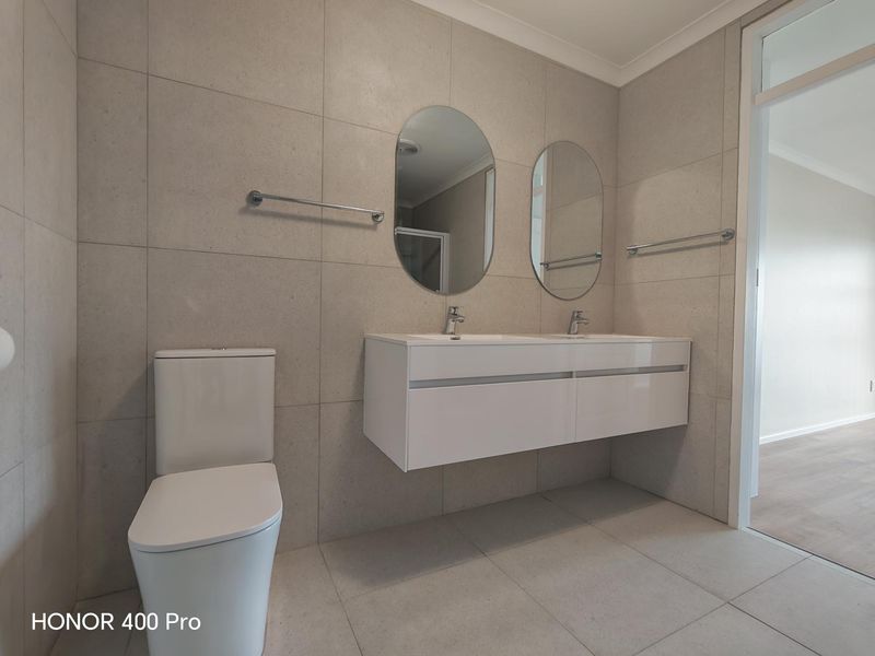 Modern bathroom featuring a double vanity with wall-mounted basins, neutral floor-to-ceiling tiling, and a contemporary toilet.
