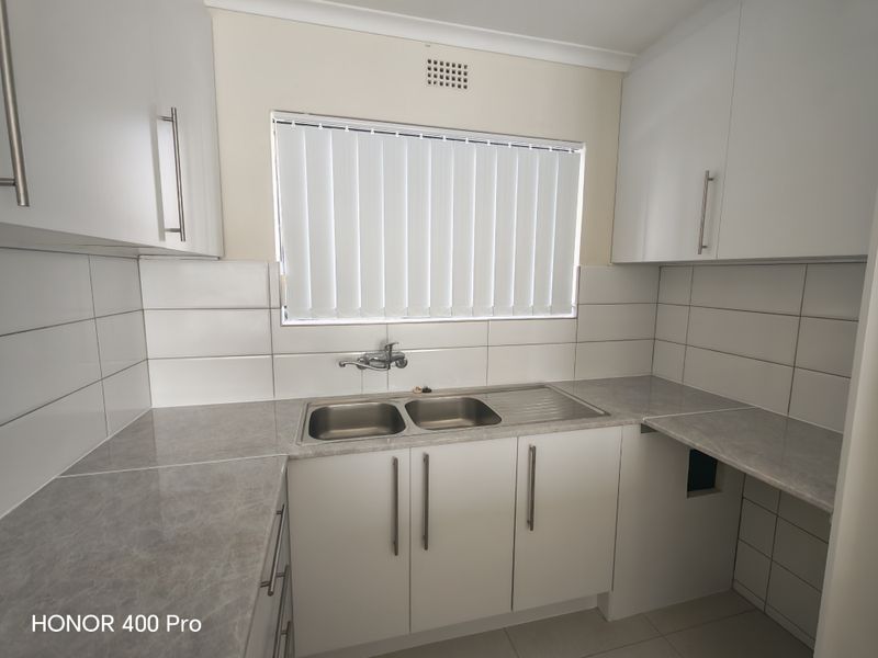 A clean, functional kitchen featuring white cabinetry, grey laminate countertops, a double stainless steel sink, and tiled splashbacks.