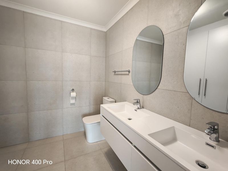 Modern bathroom featuring a sleek double vanity, wall-mounted toilet, and neutral large-format tiling throughout.