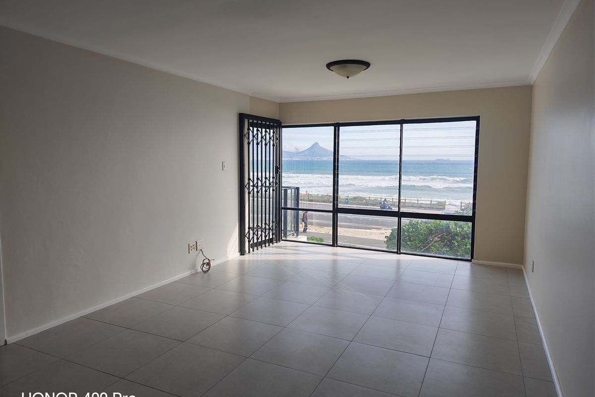 An empty, well-lit living room featuring large windows with expansive ocean and mountain views, tiled flooring, and a secure entrance gate.