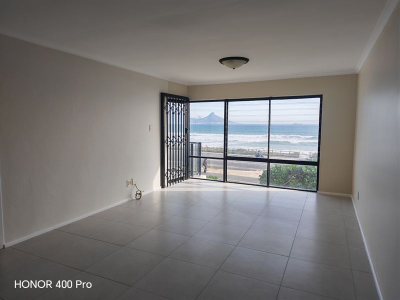 An empty, well-lit living room featuring large windows with expansive ocean and mountain views, tiled flooring, and a secure entrance gate.