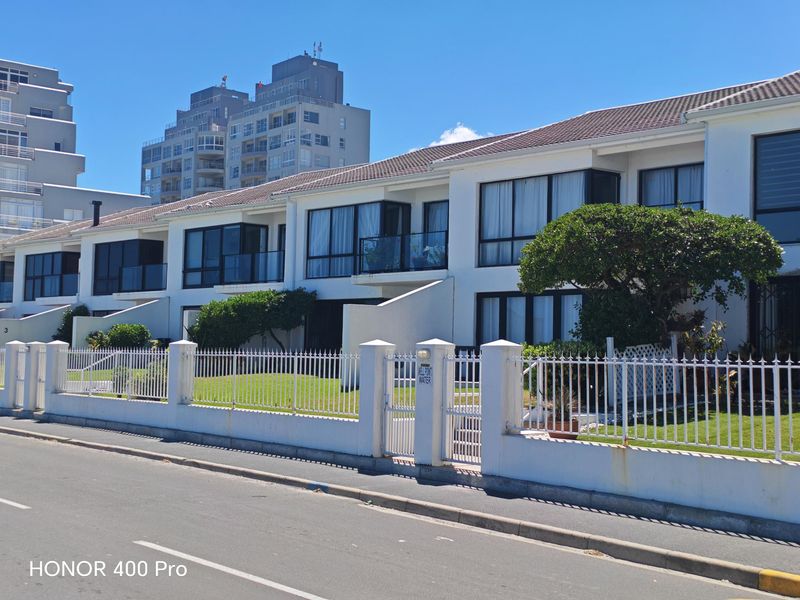 Front elevation of a multi-unit apartment complex featuring white facades, tiled roofing, private balconies, and secure metal perimeter fencing.
