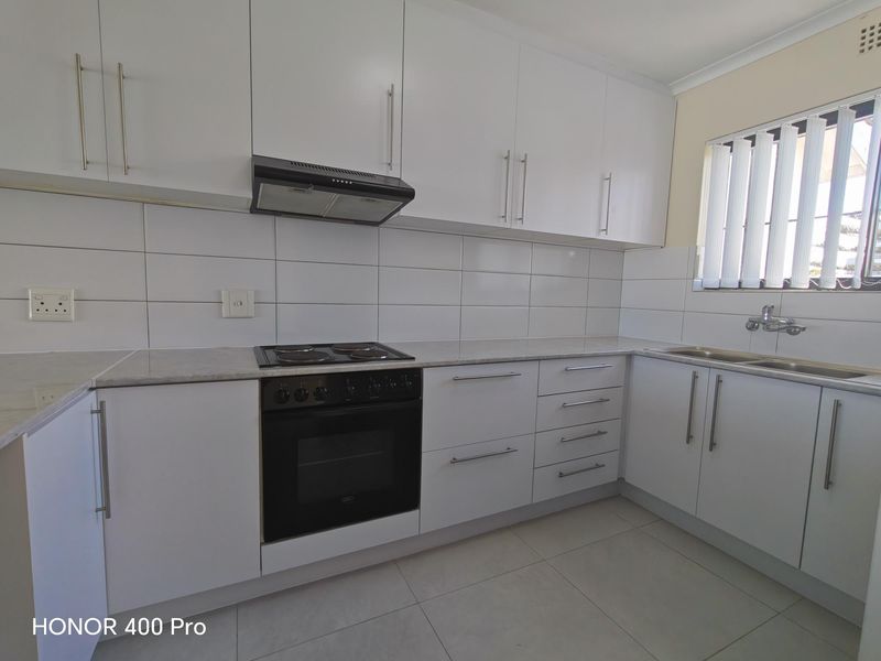 A clean, modern kitchen featuring white cabinetry, a built-in electric oven and stove, tiled backsplash, and a double sink with neutral floor tiles.