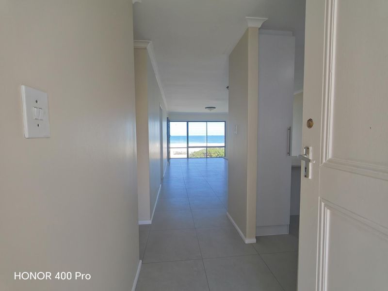 A bright, tiled entrance hallway leading into an open-plan living area with expansive ocean views through large sliding glass doors.