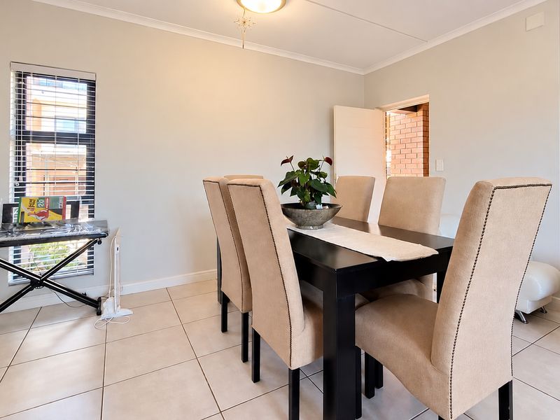 A bright dining room featuring neutral tiled flooring, a large window with blinds, and a clean, minimalist aesthetic.