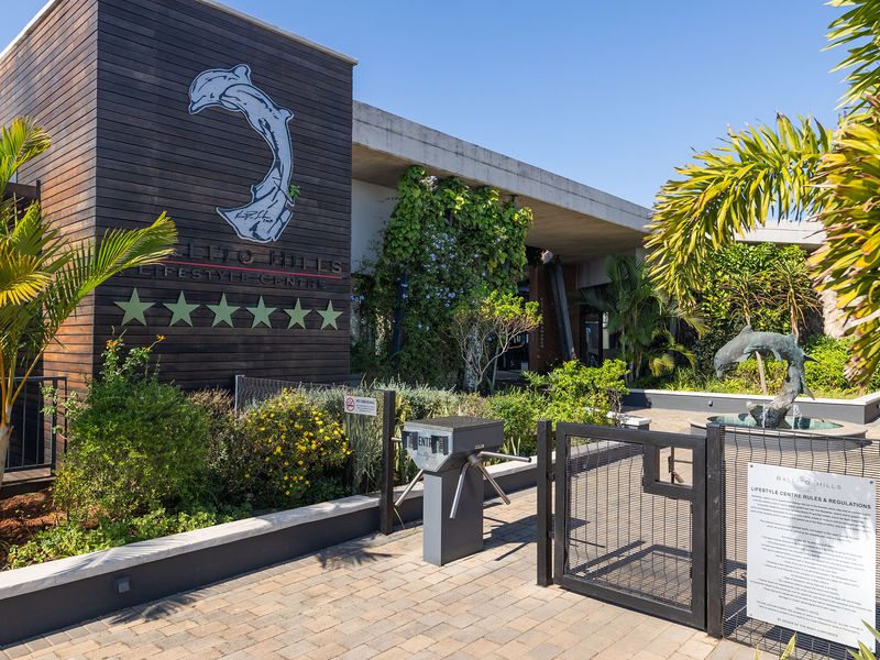 Entrance to the Ballito Hills lifestyle centre featuring a secure turnstile, paved walkway, and modern architectural timber and concrete facade.
