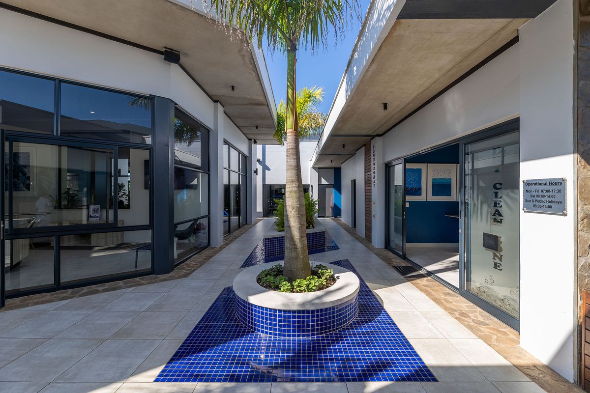 A modern, well-maintained outdoor courtyard featuring a central tiled planter box, blue mosaic accents, and glass-fronted commercial or residential units.