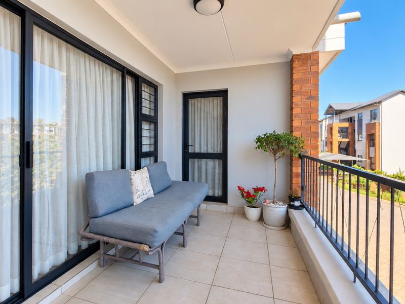 A well-maintained covered balcony featuring tiled flooring, a metal balustrade, and sliding glass door access to the apartment interior.