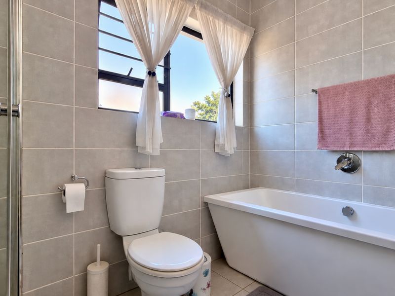 A modern bathroom featuring neutral wall tiles, a white bathtub, a separate shower enclosure, and a window providing natural light.