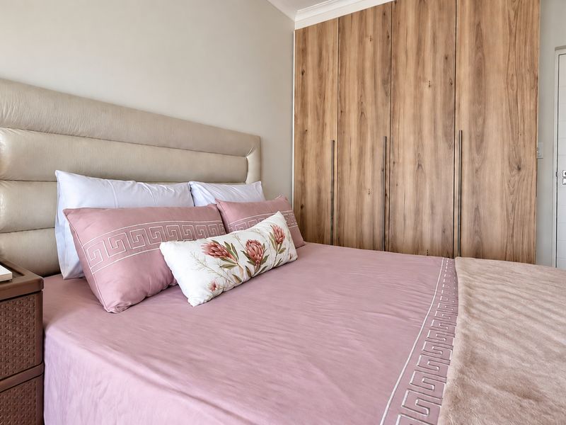 A well-maintained bedroom featuring a large built-in wooden wardrobe, an upholstered headboard, and neutral finishes.