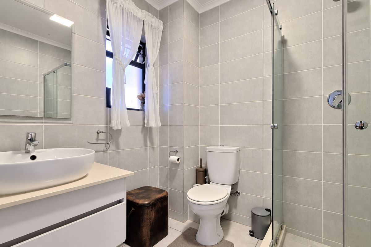 A modern, well-maintained bathroom featuring a vessel sink vanity, a glass-enclosed shower, and neutral wall tiling.