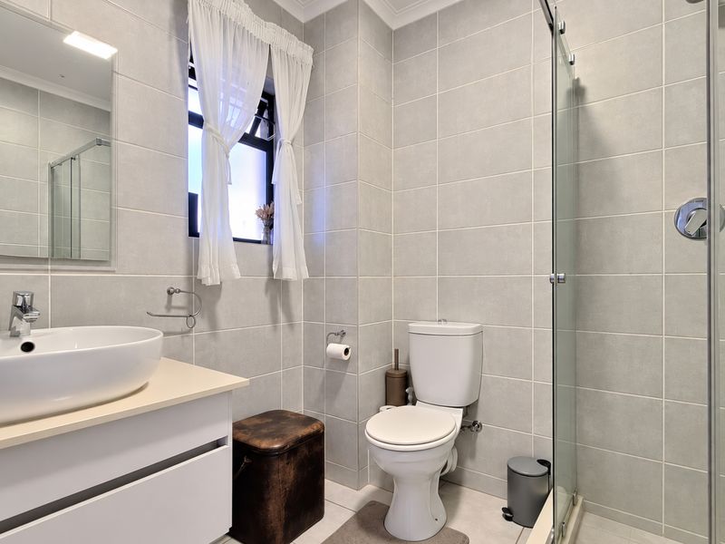 A modern, well-maintained bathroom featuring a vessel sink vanity, a glass-enclosed shower, and neutral wall tiling.