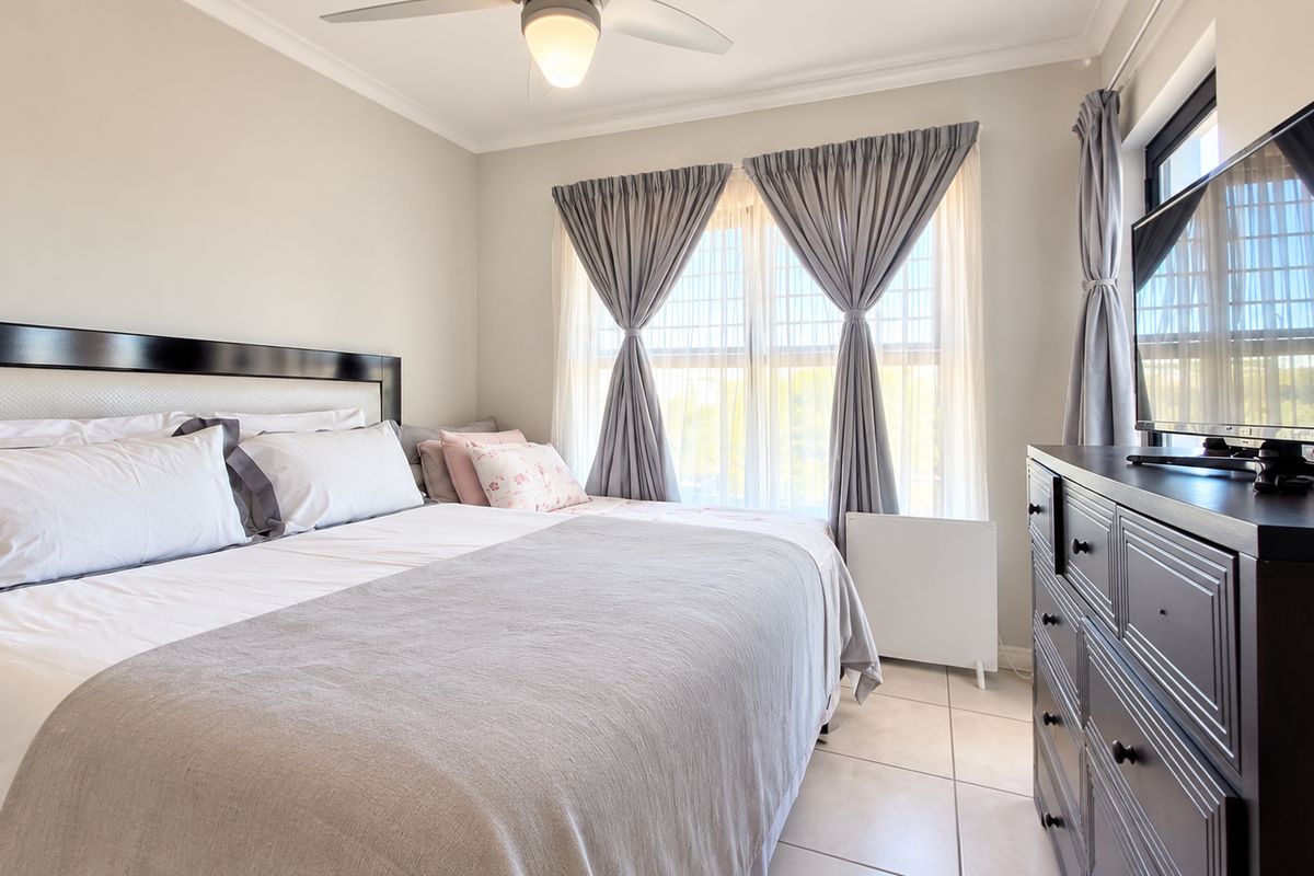 A well-maintained bedroom featuring neutral wall tones, tiled flooring, and a ceiling fan, offering a comfortable and functional living space.