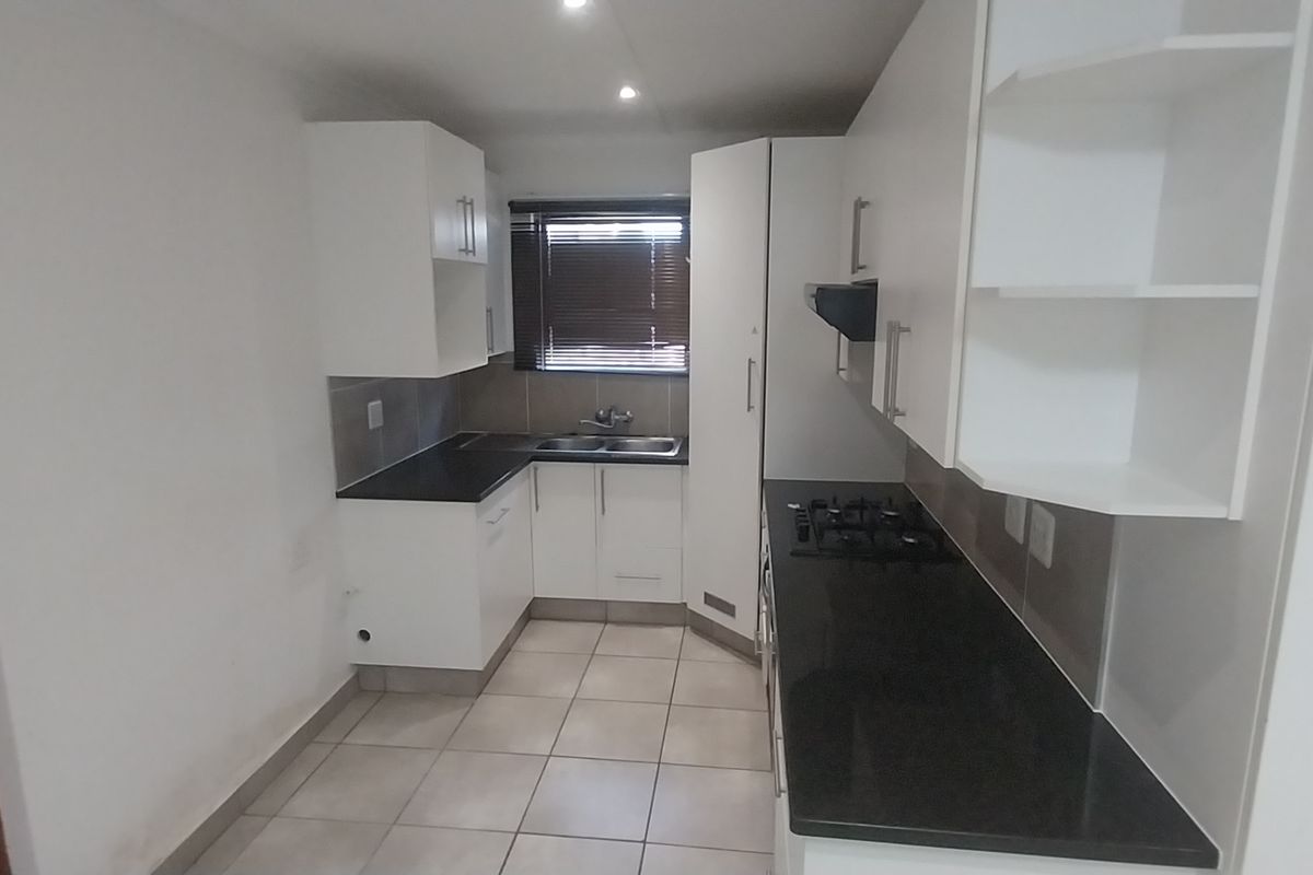 A clean, modern kitchen featuring white cabinetry, dark granite countertops, a gas hob, and tiled flooring in a functional galley layout.