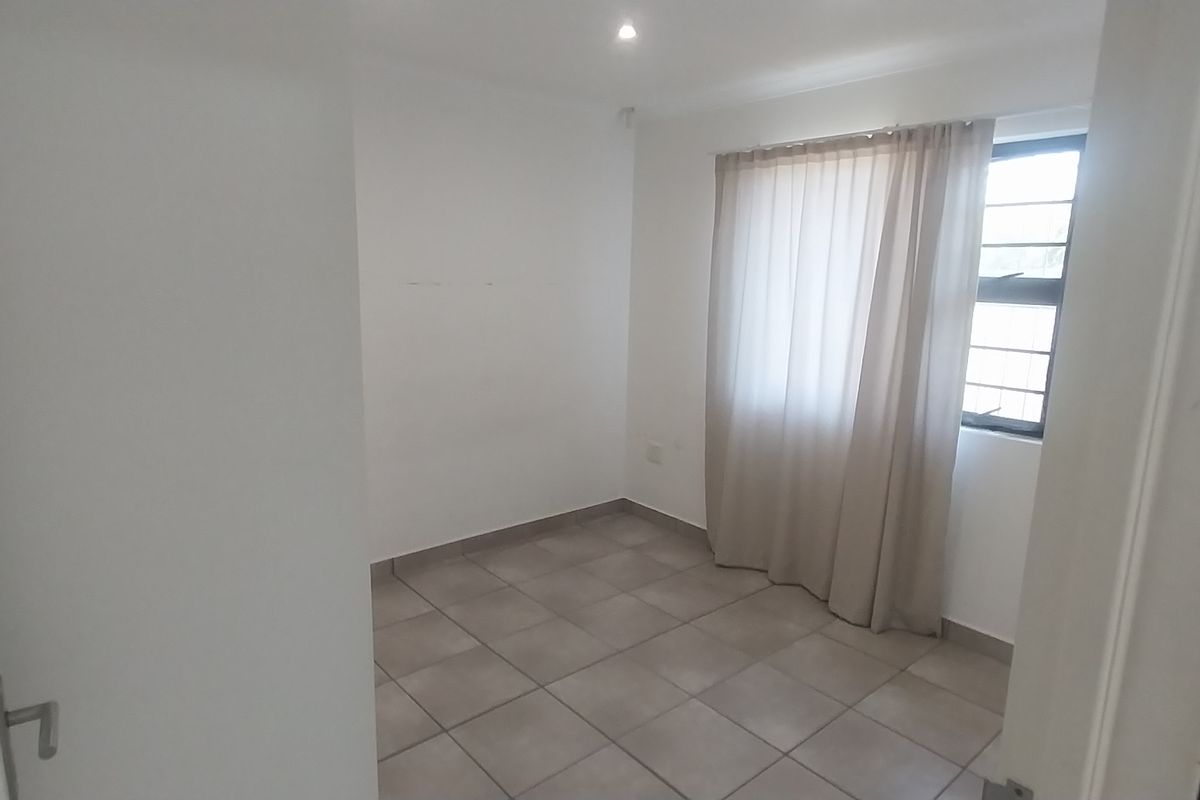 A clean, empty bedroom featuring neutral tiled flooring, recessed downlights, and a window fitted with security bars.