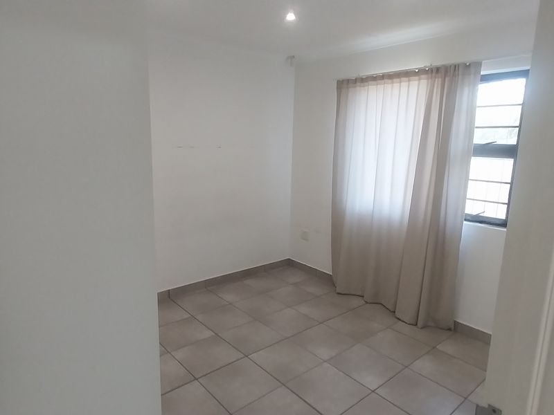 A clean, empty bedroom featuring neutral tiled flooring, recessed downlights, and a window fitted with security bars.