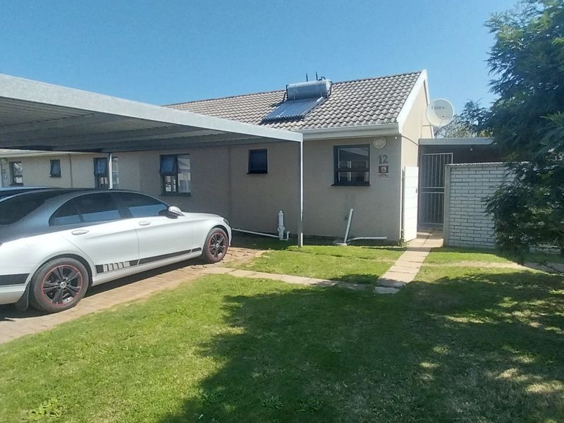 Front exterior view of the house featuring a metal carport, paved driveway, and a solar water heating system installed on the tiled roof.