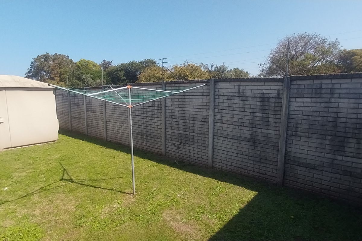 A rear garden area featuring a lawn and enclosed by high brick and precast concrete boundary walls.