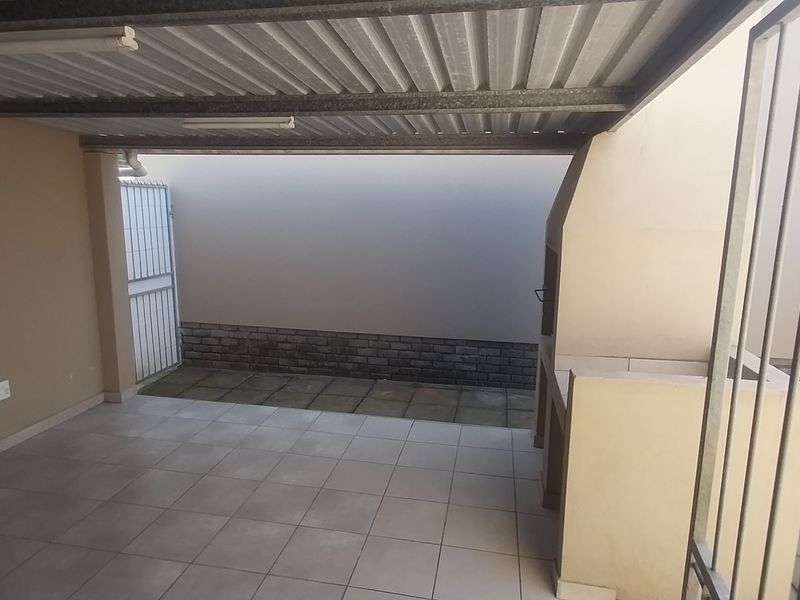 A covered outdoor patio area featuring a built-in braai, tiled flooring, and a corrugated metal roof, providing a functional space for outdoor entertaining.