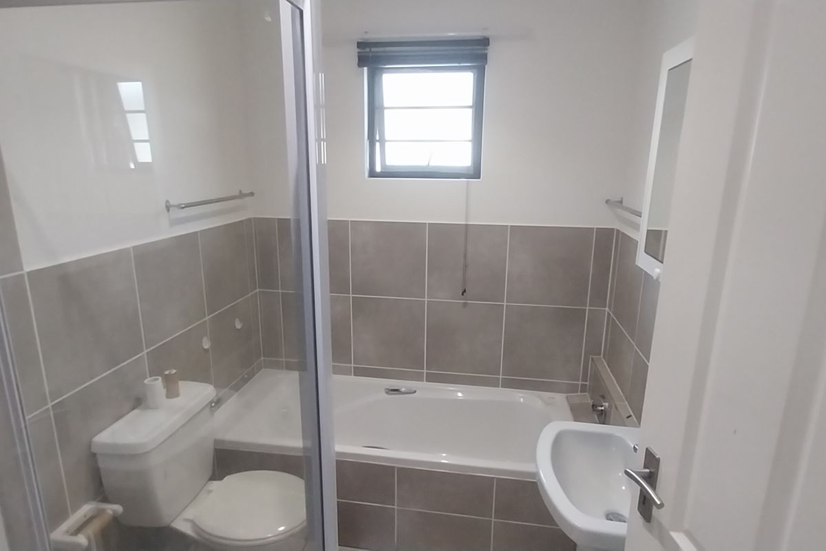 A clean, functional bathroom featuring a bathtub, separate shower enclosure, pedestal basin, and neutral wall tiling.