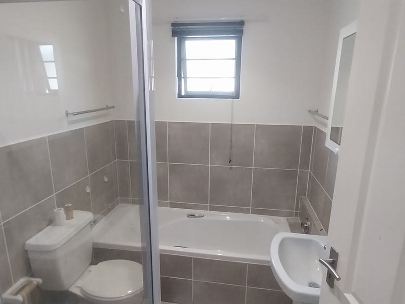A clean, functional bathroom featuring a bathtub, separate shower enclosure, pedestal basin, and neutral wall tiling.