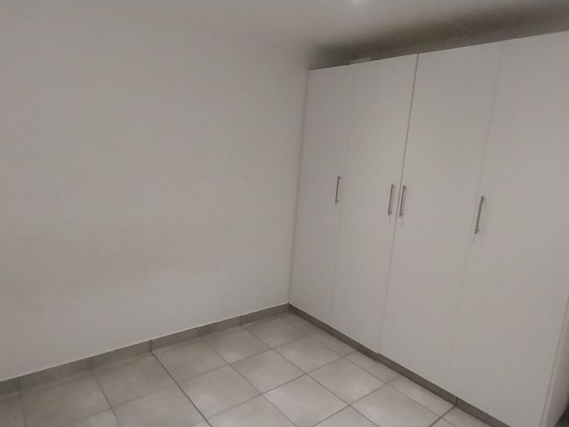 A clean, empty bedroom featuring neutral tiled flooring and a large, white built-in wardrobe.