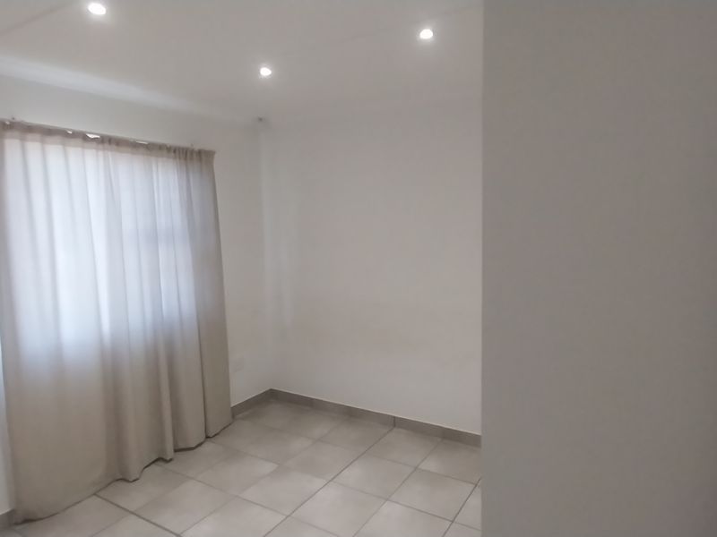 A clean, empty bedroom featuring neutral tiled flooring and recessed downlighting, providing a blank canvas for personalization.